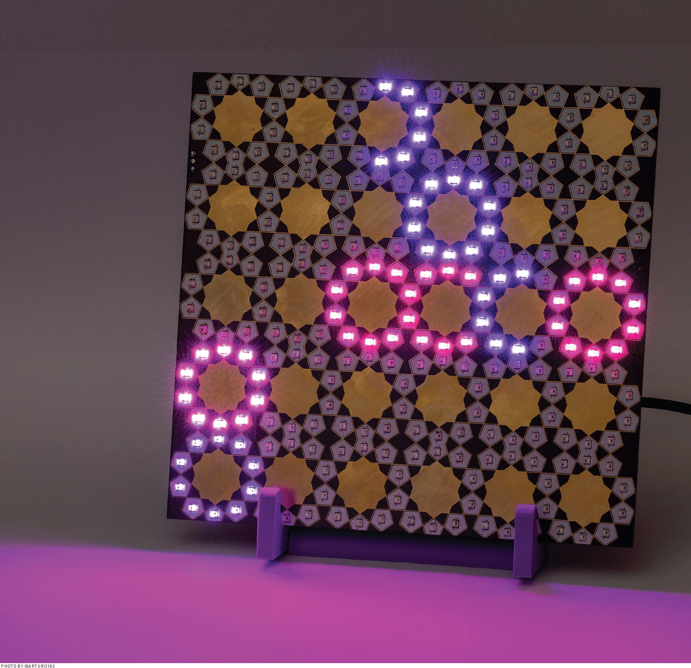 A printed circuit board for visualizing moon phases and a menstruation cycle. The board's design consists of LEDs arranged in Islamic geometry patterns with circular units in a 6x5 grid (30 units). Some LED units are lit to show the moon phases in purple and menstruation days in pinkish red.